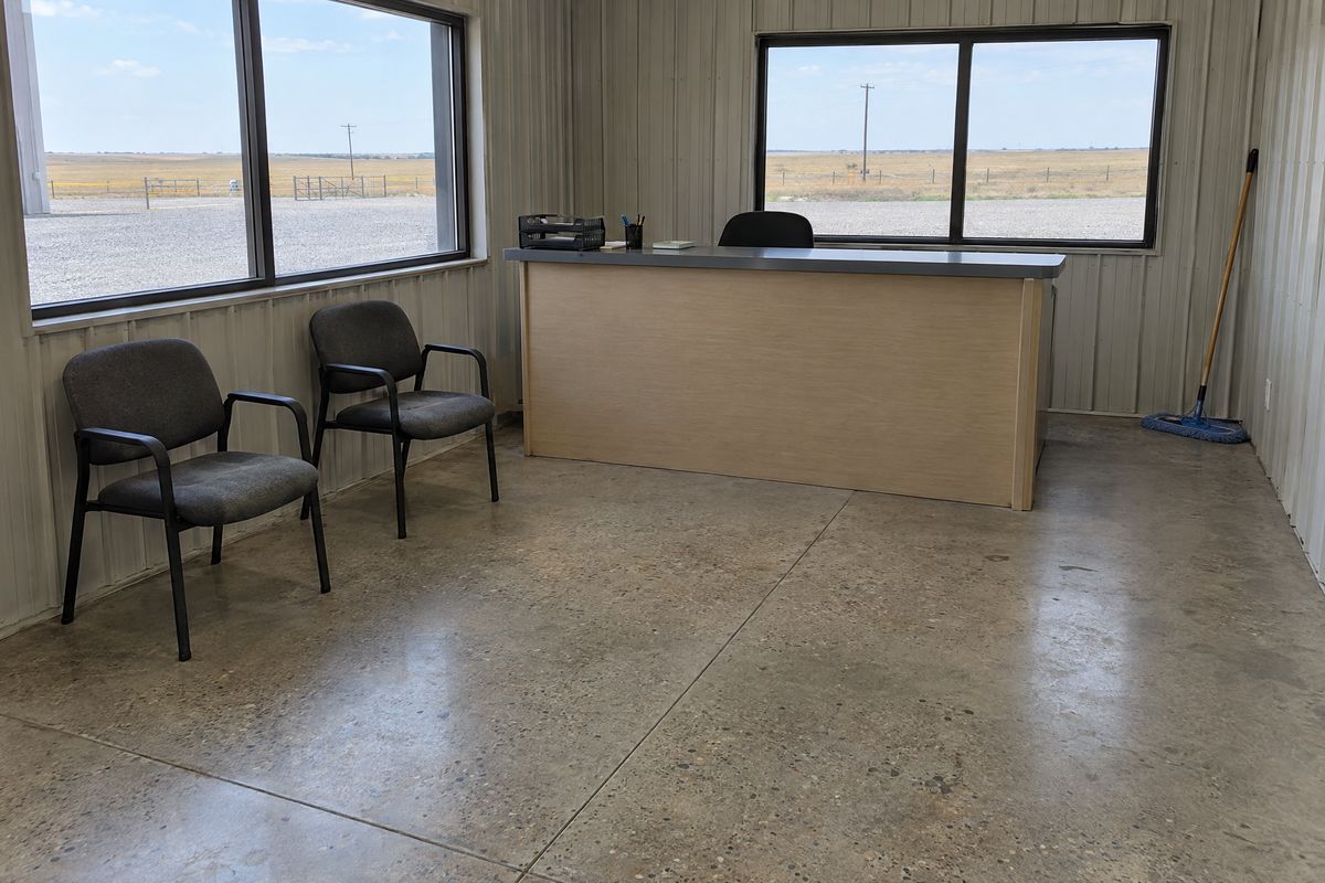 Office and counter room in a metal building with a low-sheen polished concrete floor, fine aggregate, a saw-cut joint, a dust mop and windows to flat land.