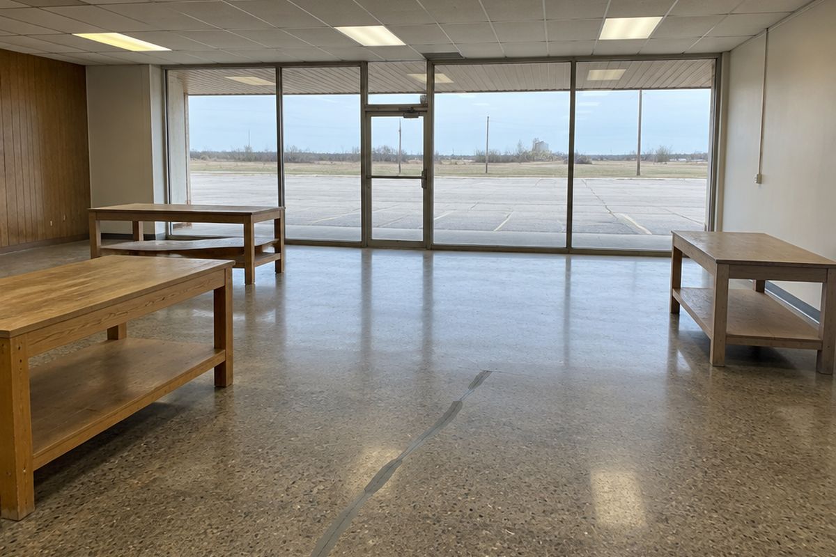 Empty small store with a medium-sheen polished concrete floor, salt-and-pepper aggregate, a long gray-filled crack, plain display tables and a glass storefront.